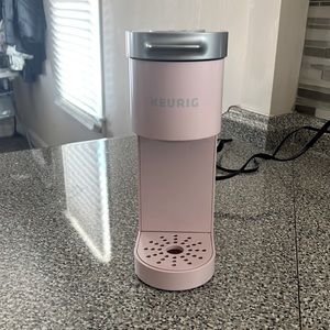 Single cup pink kurig coffee maker with black spinning carousel for pods.